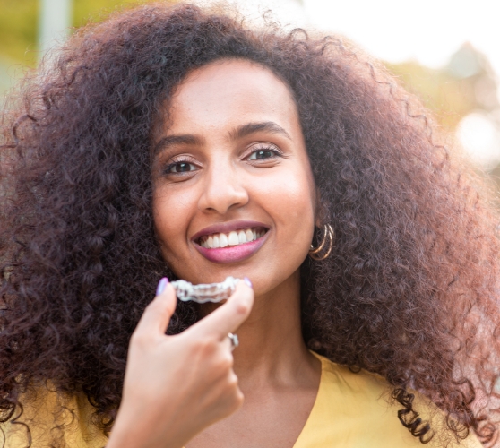 Smiling woman holding an Invisalign clear aligner