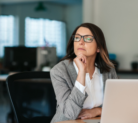 Woman sitting at desk with laptop and looking contemplative