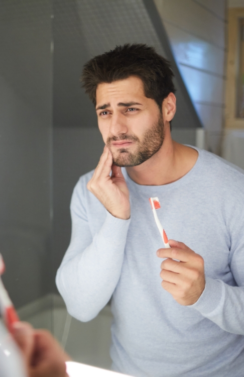 Man with tooth pain looking in mirror needing emergency dentist in Easton