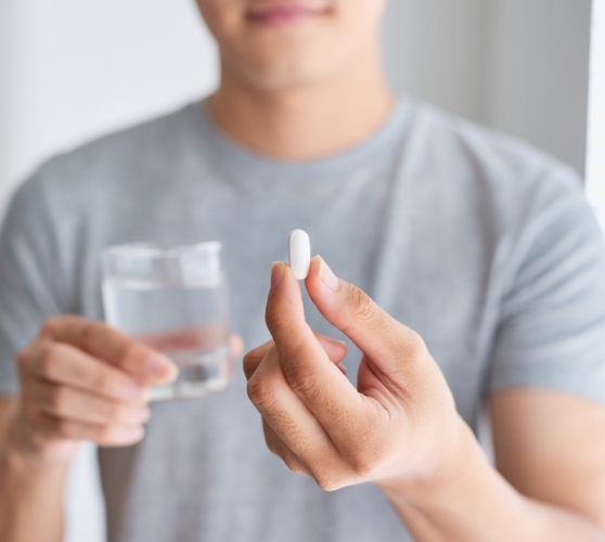 Person holding a white pill and a glass of water