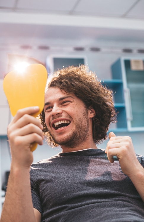 Young man looking at his smile in mirror after receiving dental services in Easton