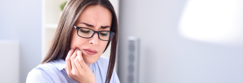 Woman wincing and holding the side of her jaw in pain