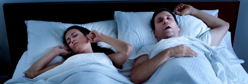 Woman laying in bed frustrated next to snoring man