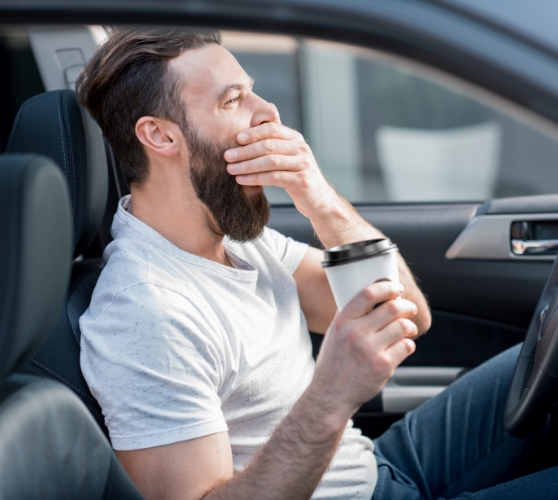 Man in driver seat of car covering his mouth while yawning